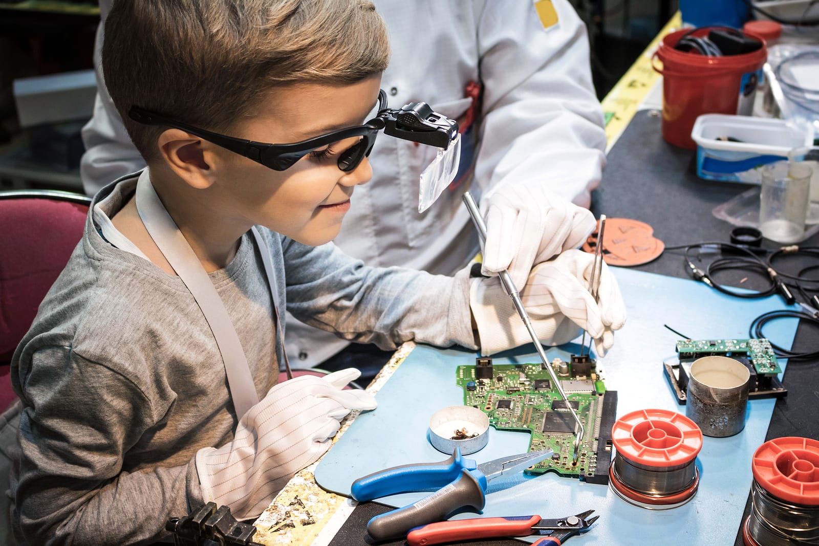 Student wearing safety glasses working on an electronics circuit board with an instructor